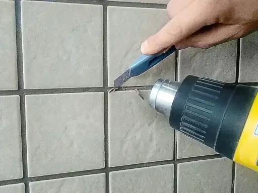 Usuwanie starej fugi epoksydowej na zewnątrz za pomocą opalarki i nożyka.