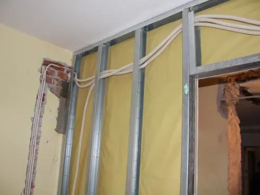 Trwa wymiana instalacji elektrycznej w mieszkaniu. Widać metalowy stelaż, żółtą membranę i nowe przewody elektryczne w peszlach.