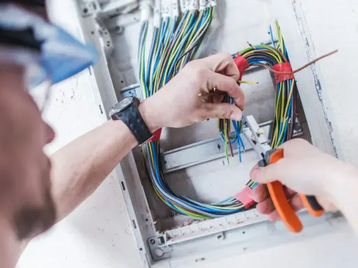 Elektryk pracuje nad prostą instalacją elektryczną, przycinając kolorowe przewody w skrzynce rozdzielczej.