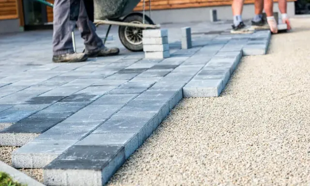 Układanie betonowych płyt na żwirze. Pracownicy tworzą nowoczesny taras, gdzie beton zamiast kostki brukowej stanowi estetyczne i trwałe rozwiązanie.