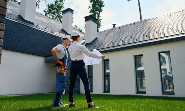 Architekt i budowlaniec omawiają plany domu. Czy można mieszkać w domu bez odbioru? To pytanie, na które odpowiedź znajdą, analizując projekt.