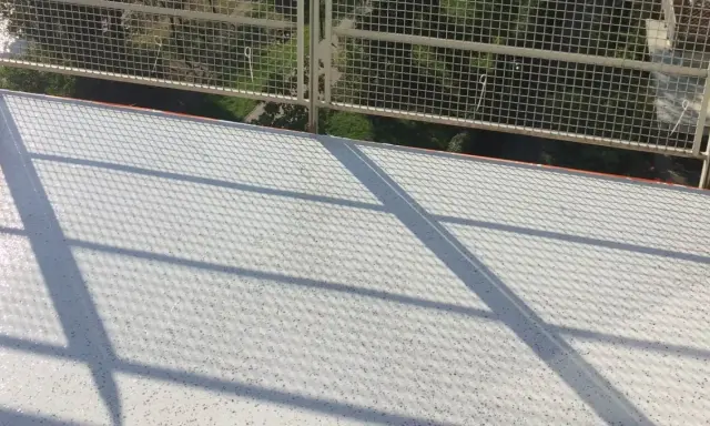 Nowy, biały balkon z żywicą, lśniący w słońcu. Cienie siatki tworzą ciekawy wzór na jego powierzchni.