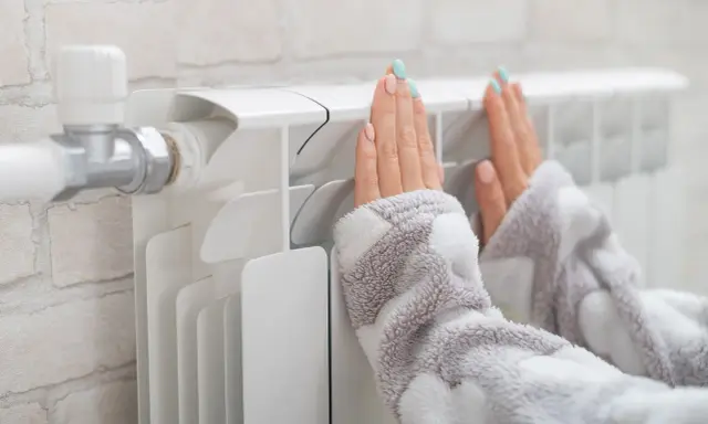 Dłonie ogrzewają się przy grzejniku, który ma podłączenie od dołu.