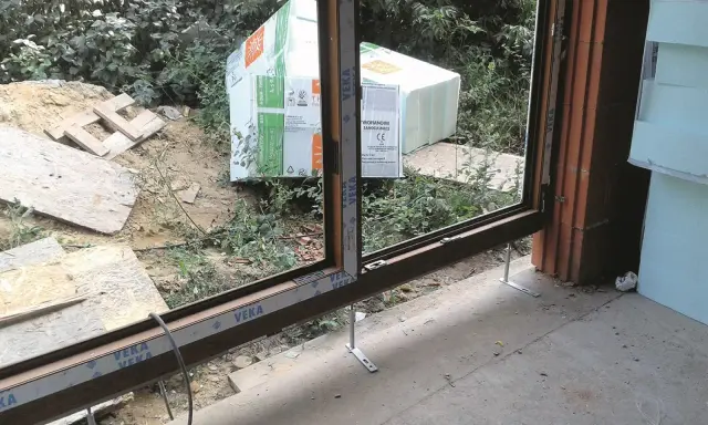 Próg drzwi tarasowych w trakcie montażu, przygotowany do ocieplenia progu. W tle materiały budowlane i zieleń.