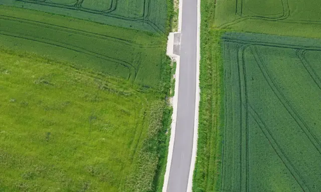 Asfaltowa droga dwukierunkowa przecina zielone pola. Minimalna szerokość drogi zapewnia płynny ruch.