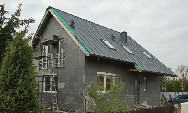 Przebudowa starego domu projekty: szary dom w trakcie budowy, z nowym dachem, oknami i rusztowaniami.
