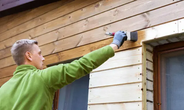 Mężczyzna maluje deskę elewacyjną, tworząc piękne aranżacje drewnianego domu.
