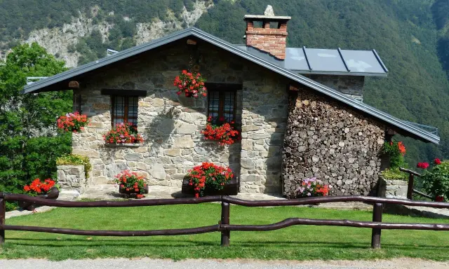 Kamienny domek letniskowy z kwitnącymi pelargoniami. Marzenie o własnym miejscu na ziemi, być może z dofinansowaniem na domek letniskowy, staje się rzeczywistością.