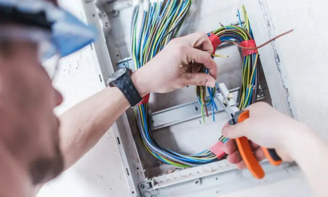 Elektryk pracuje nad prostą instalacją elektryczną, przycinając kolorowe przewody w skrzynce rozdzielczej.