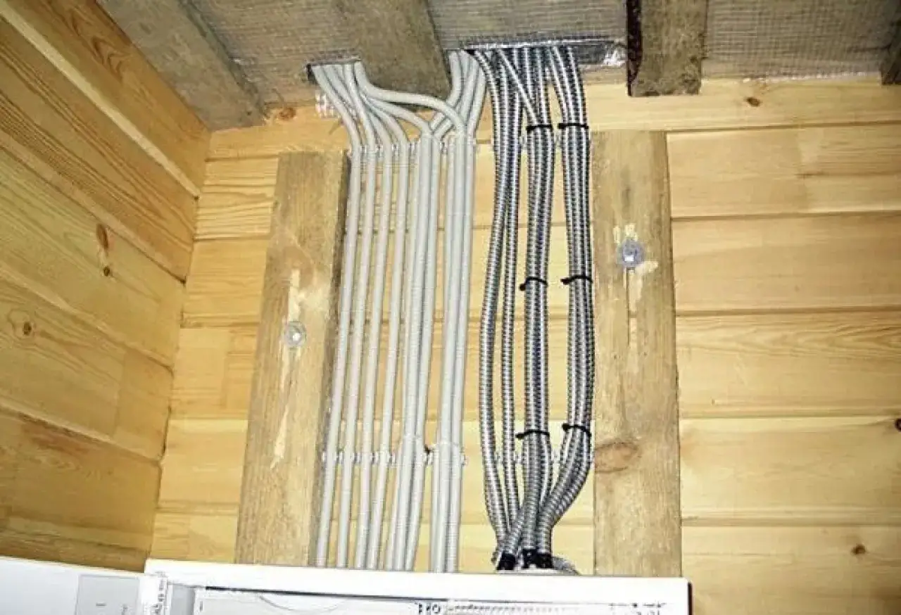 Instalacja elektryczna w domu drewnianym schemat: wiązki kabli w peszlach wychodzące z sufitu i biegnące wzdłuż drewnianych ścian.