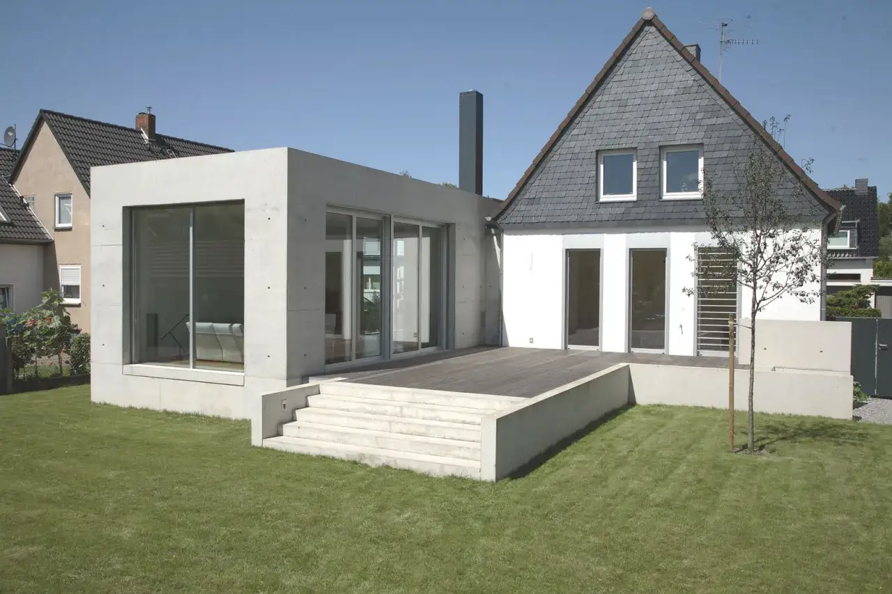 Nowoczesna dobudówka do starego domu, z betonu i szkła, kontrastuje z tradycyjną architekturą. Projekty uwzględniające takie połączenia są coraz popularniejsze.