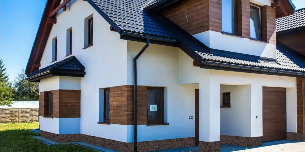 Nowoczesny dom z białym tynkiem i drewnianymi akcentami. Zastanawiasz się, cokół co to? To ta ozdobna, kamyczkowa warstwa u podstawy budynku.