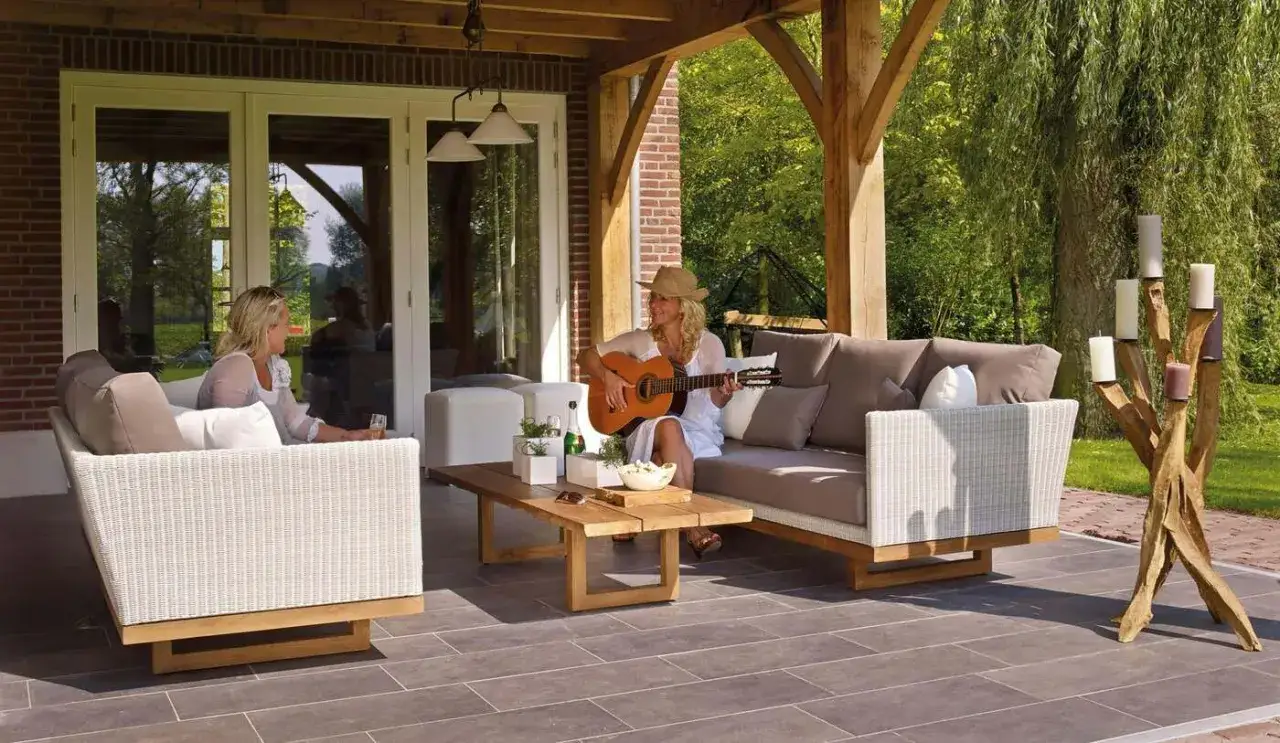 Kobieta gra na gitarze na zadaszonym tarasie, obok niej siedzi przyjaciółka. To idealne miejsce na relaks, jak balkon w letni dzień.