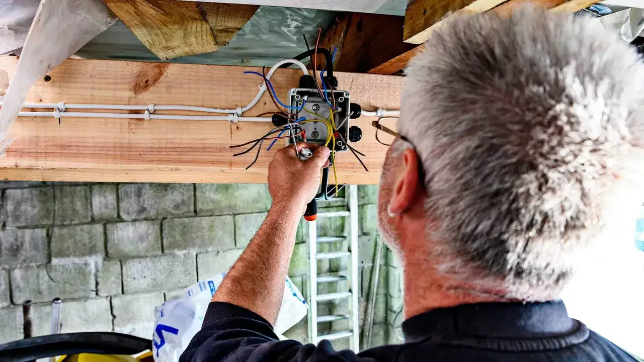 Mężczyzna wykonuje instalację elektryczną w garażu, łącząc przewody w puszce.